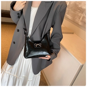 Glossy black underarm bag with a gold metal bow buckle shown on a model's shoulder