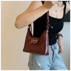 Nahaufnahme der weinroten Lackleder-Tasche mit silberner Schleife und Knotendetail am Gurt