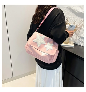 Pink canvas messenger bag with white plush stars shown on a model in a minimalist setting