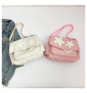 Flat lay detail of cream and pink nylon messenger bags with star patches and adjustable straps