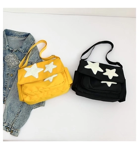 Detailed view of yellow and black messenger bags with plush star patches on white base