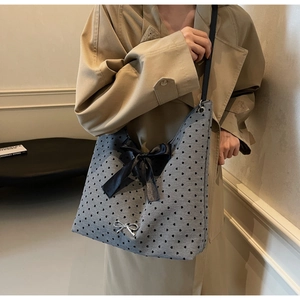 Close-up of grey knit tote bag featuring black hearts, satin bow, and metallic charm