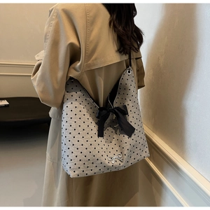Detail of grey polka dot tote bag with large black bow on a model in a beige trench coat