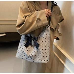 Detail of grey polka dot tote bag with large black satin bow and silver charm