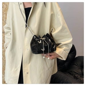 Detail of black drawstring bucket bag with silver butterfly studs and pearl charms