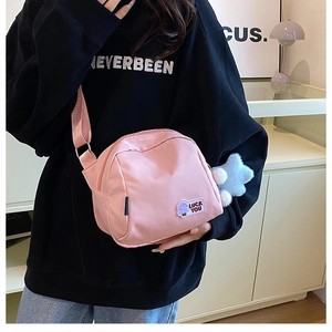 Pink nylon crossbody bag with embroidery detail and plush charm worn by model