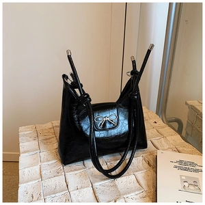 Elegant black glossy bow shoulder bag with silver hardware on a textured stone surface