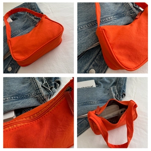 Detail view of bright orange nylon baguette bag showing zipper and interior capacity