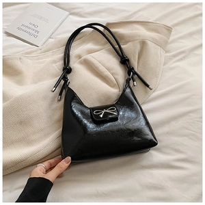 Detail of black glossy leather underarm bag with metal bow buckle and knotted straps