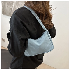 Detailed side view of a light blue nylon hobo bag worn by a model in a minimalist setting