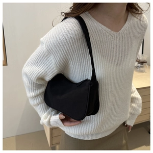 Close-up of minimalist black nylon crescent shoulder bag worn with a white knit sweater