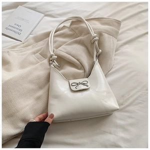Detail of cream leather shoulder bag featuring a silver bow buckle and knotted strap