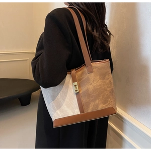 Detail of canvas tote bag with brown leather trim and golden metal lock hardware