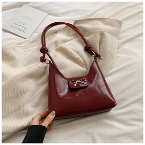 Close-up of wine red glossy leather shoulder bag with a metal bow buckle and knot strap
