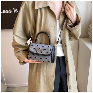 Detailed side view of grey polka dot handbag with golden bow lock on khaki trench coat