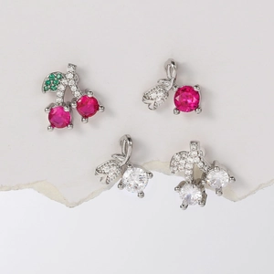 Macro shot of silver cherry earrings with red and green zircon gemstones on white stone