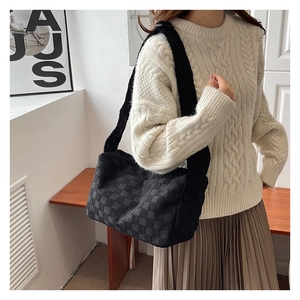 Close-up of black woven tote bag with checkerboard pattern worn with a knit sweater