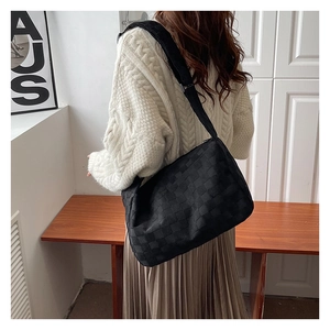 Detail of black woven crossbody bag featuring textured checkerboard pattern and wide strap