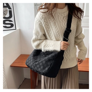 Detail of black woven texture shoulder bag worn with a white knit sweater