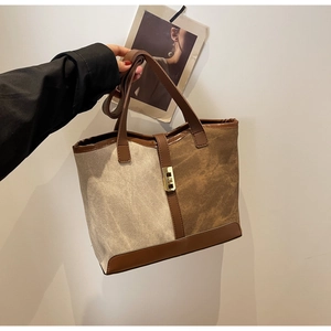 Contrast color canvas tote bag with leather trim and gold twist-lock closure in hand