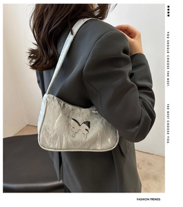 Detail of silver pleated shoulder bag with metallic butterfly and sleek zipper