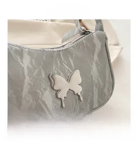 Detail shot of silver butterfly ornament on grey textured leather underarm bag with zipper