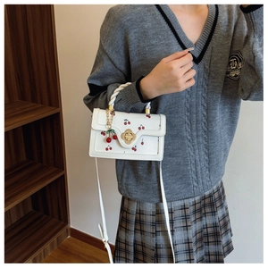 White crossbody bag with cherry prints, twist handle, and a gold flower lock