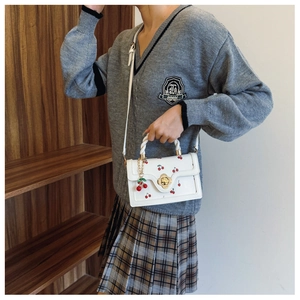 Detail van witte crossbodytas met kersenprint en gouden metalen bloemvormige sluiting