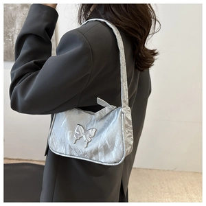 Silver pleated underarm bag with metal butterfly detail worn by model in grey suit
