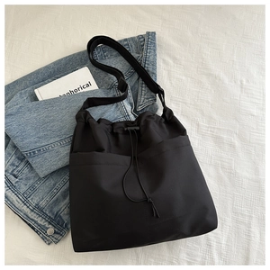 Detail of black drawstring bucket bag with adjustable strap on denim jacket