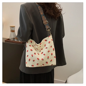 Detail of strawberry bucket bag with embroidered wide strap and golden hardware