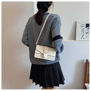 Detail of a beige PU leather crossbody bag with brown monogram pattern and golden M clasp