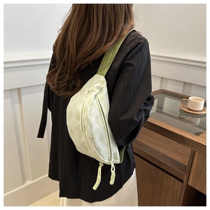Close-up of light green textured crossbody bag with dual zippers and woven details