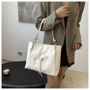 White ballet-style tote bag with bow detail and twisted shoulder straps on a model