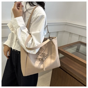 Detail of a beige tote bag with a bow accent and twisted strap in a minimalist style