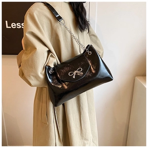 Close-up of black patent leather shoulder bag with silver bow accent on model