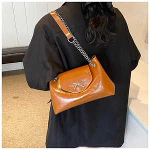 Rear view of model wearing a glossy brown leather shoulder bag with silver bow accent