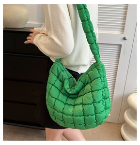 Detail of green quilted puffer tote bag on shoulder with thick padded strap and soft texture