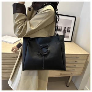 Detail of black PU leather tote with metal eyelets, bow accents and braided straps