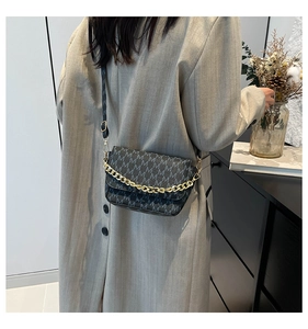 Detail view of dark grey crossbody bag with M-pattern and decorative gold chain