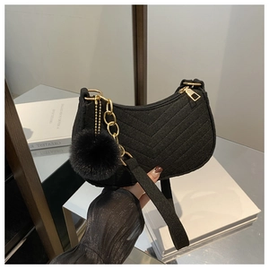 Detail of black V-quilted hobo bag with gold chain and plush ball charm accessory
