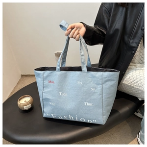 Detailed close-up of light blue denim tote bag featuring red and white weekday typography