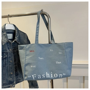 Detail of light blue denim tote bag featuring white Fashion text and weekday prints