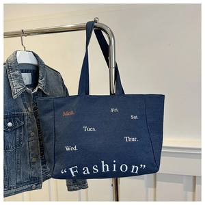 Detail of dark blue denim tote bag featuring white Fashion lettering and weekday text