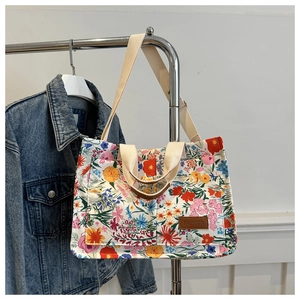 Detail view of floral canvas tote bag featuring brown leather FASHION label and woven strap