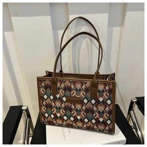 Detail of colorful geometric woven tote bag with brown faux leather straps on a white book