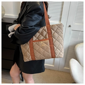 Close-up of khaki quilted tote bag with orange canvas straps and metal snap pocket
