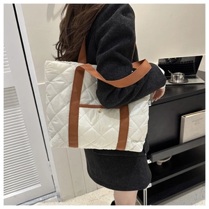 Detail view of large white quilted tote bag with brown straps and gold button on model