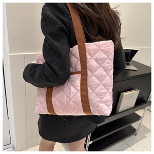 Detailed side view of pink quilted tote bag with brown straps worn by a model