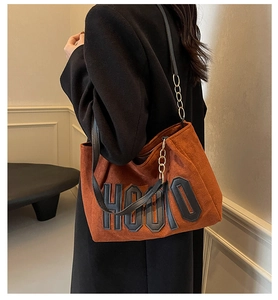 Detail of brown suede tote bag with black HOOTO lettering and gold chain handle detail